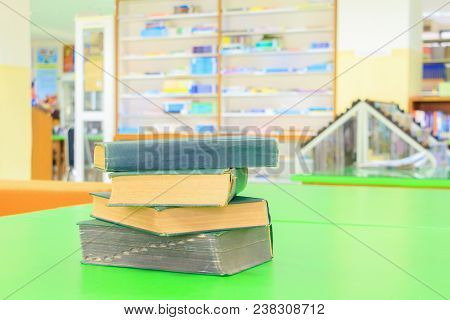 Old Book And Heap Treatise In School Library On Table Green. Blurry Bookshelves Background. Educatio