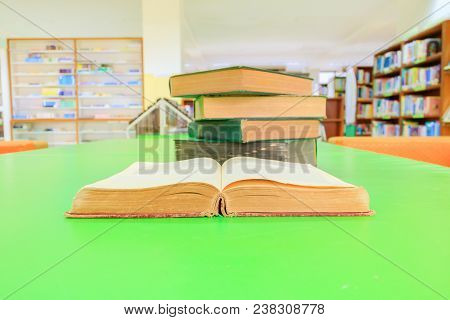 Open Old Book And Heap Treatise In School Library On Table Green Blur Bookshelves Background. Educat
