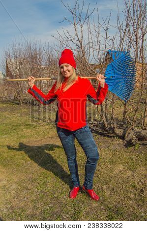 Full Length Portrait Of A Smiling Woman Professional Gardener With A Rake, A Beautiful Blonde Workin