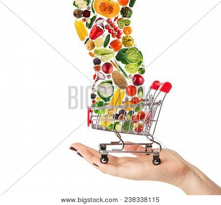 Female Hand Holding Grocery Cart With Vegetables And Fruits Falling In It Isolated On White. Healthy