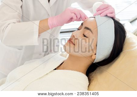 Portrait Of Pretty Asian Woman Enjoying Beauty Treatment In Spa With Cosmetologist  Performing Facia