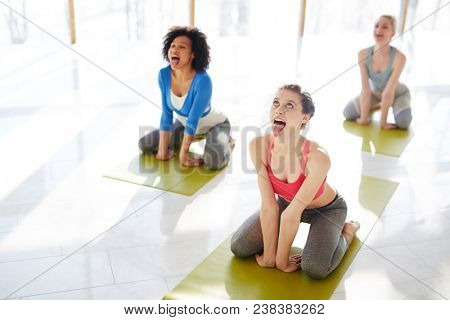 Three young females in simhasana posture rolling their eyes and sticking out tongues on mats