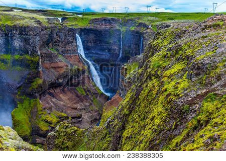  The concept of extreme and phototourism. High waterfall Hayfoss in a picturesque and dangerous tundra canyon. Cloudy and windy summer day in Iceland