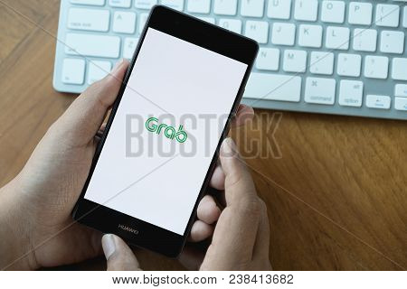 Chiang Mai,thailand - Mar 28,2018 : A Man Hand Holding Grab App Showing On Huawei P10 On Wooden Tabl