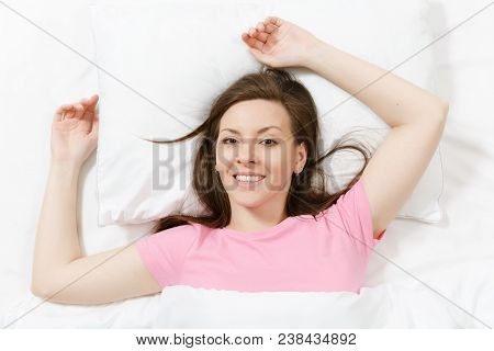 Top View Of Happy Brunette Young Woman Lying In Bed With White Sheet, Pillow, Blanket, Hands Under H