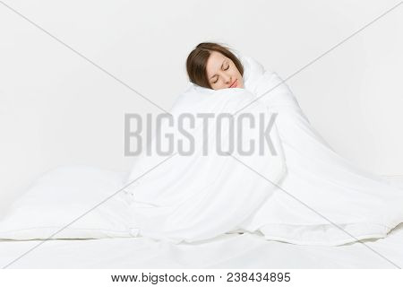 Young Brunette Woman Sitting In Bed With White Sheet, Pillow, Wrapping In Blanket On White Backgroun