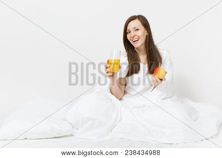 Young Brunette Woman Sits On Bed With White Sheet, Pillow, Wrapping In Blanket Isolated On White Bac