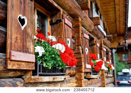 Typical Bavarian Or Austrian Wooden Window With Red Geranium Flowers On House In Austria Or Germany.