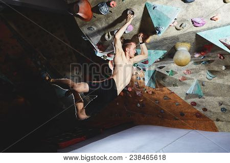 Workout Exercise. Top View Of A Man Climber Climbs Indoors In Bouldering Gym. Athletic Man Climbing 