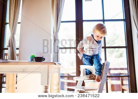 Unrecognizable Little Toddler Boy Climbing Into Wooden Highchair At Home. Domestic Accident. Dangero