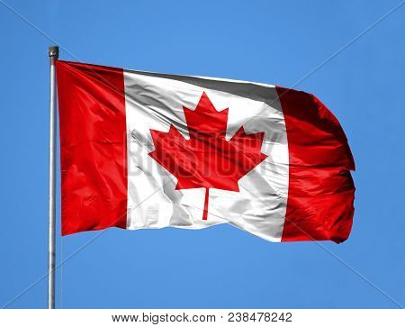 National Flag Of Canada On A Flagpole In Front Of Blue Sky.