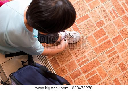 A Boy Is Tying The Shoelaces To Prepare To Go To School In The Morning At Home Hastily. Copy Space F