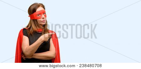 Middle age super hero woman wearing red mask and cape pointing away side with finger isolated blue background