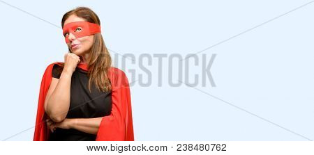 Middle age super hero woman wearing red mask and cape thinking and looking up expressing doubt and wonder isolated blue background
