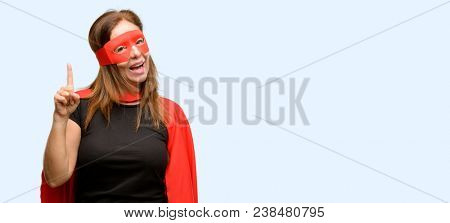 Middle age super hero woman wearing red mask and cape pointing away side with finger isolated blue background