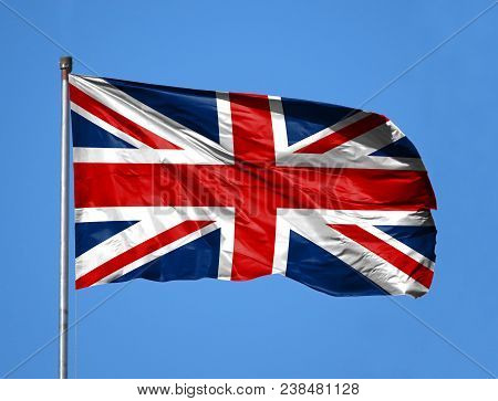 National Flag Of United Kingdom On A Flagpole In Front Of Blue Sky.