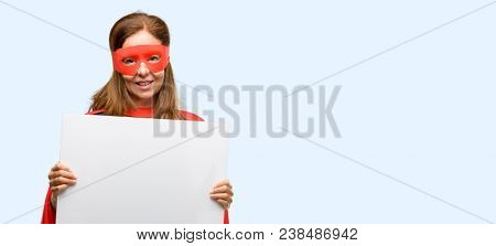 Middle age super hero woman wearing red mask and cape holding blank advertising banner, good poster for ad, offer or announcement, big paper billboard isolated blue background