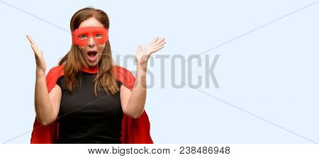 Middle age super hero woman wearing red mask and cape happy and surprised cheering expressing wow gesture isolated blue background