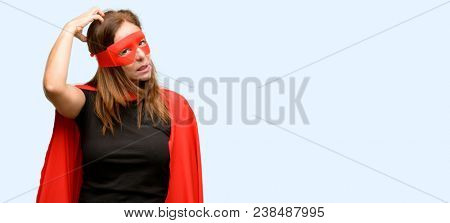 Middle age super hero woman wearing red mask and cape doubt expression, confuse and wonder concept, uncertain future isolated blue background
