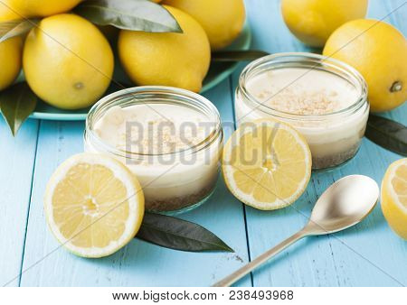 Glass Jar With Lemon Cheesecake With Fresh Lemons On Bluw Wooden Background