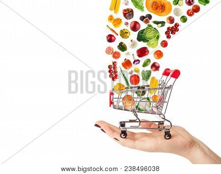 Female Hand Holding Grocery Cart With Vegetables And Fruits Falling In It Isolated On White. Healthy