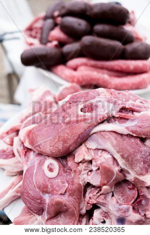 closeup of a pile of slices of raw pork and lamb meat and some raw sausages in the background