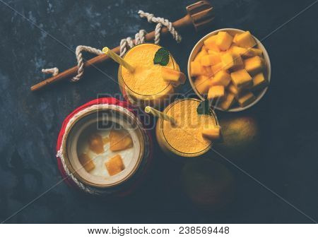 Mango Lassi Or Smoothie In Big Glass Or Small Bottles With Curd, Cut Fruit Pieces And Blender. Moody