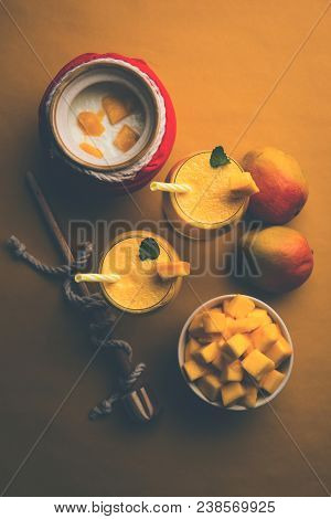 Mango Lassi Or Smoothie In Big Glass Or Small Bottles With Curd, Cut Fruit Pieces And Blender. Moody