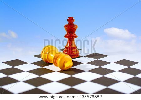 Two Chess Kings On Board, One Standing, One Lying Down, Blue Sky And White Clouds Background. Looks 