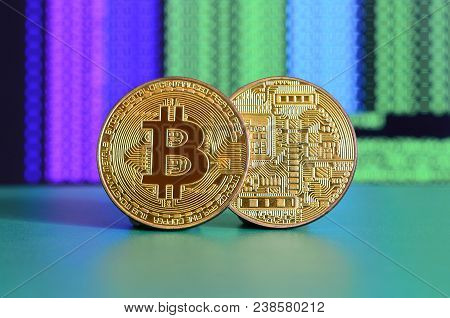 Two Gold Bitcoins Lie On The Green Surface On The Background Of The Display, Which Shows The Process