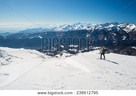 Tour Skier Hiking Uphill On Snowy Slope Under A Bright Sun With Clear Deep Blue Sky. Scenic Setting 