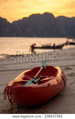 A Red Canoe On A Beach With A Golden Hour Sunset Over The Mountains In The Background. The Beach Is 