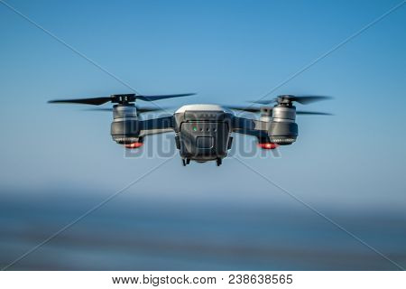 A Dji Spark Drone In Color Alpine White Mid-air Flying Over The Water With The Blue Sky In The Backg