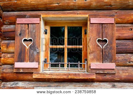 Typical Bavarian Or Austrian Wooden Window With Red Geranium Flowers On House In Austria Or Germany.