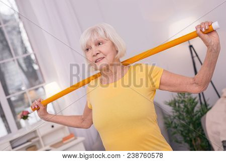 Useful Tool. Beautiful Woman Exercising With A Health Wand, Holding It Behind Her Back And Smiling P