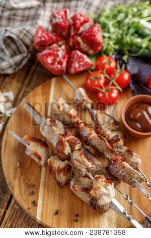 Shish Kebab From Pork On A Wooden Background. Appetizing Meat Cooked On An Open Fire And Fresh Veget
