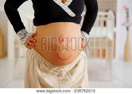 Close-up of pregnant belly with drawn smiley face.