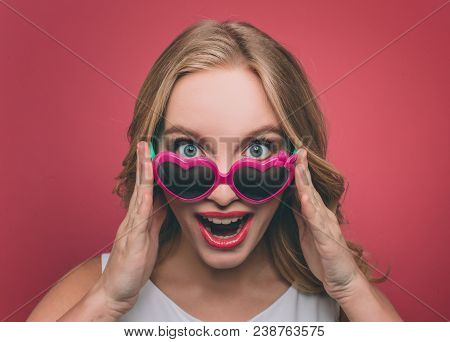 Pretty Woman With Blonde Hair Weard Sunglasses With Pink Edge. She Is Looking On Camera And Holding 