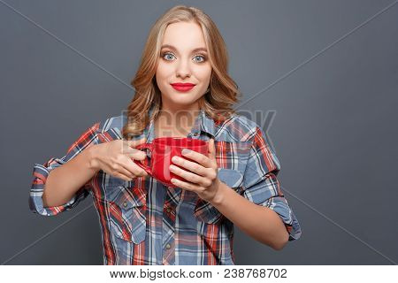 Nice Blonde Girl Is Holding A Red Cup And Looking Straight Forward. She Is Going To Drink From The C