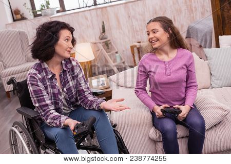 Innovative Fun. Optimistic Incapacitated Woman And Girl Holding Controller While Looking At Each Oth