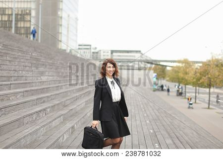 Female Secretary Standing On Stairs With Bag And High Buildings In Background. Concept Of Profession