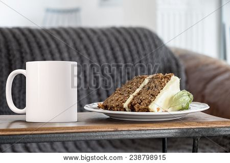 White Blank Coffee Mug Mock Up. The Mug Is Next To A Piece Of Carrot Cake With A Sofa In The Backgro