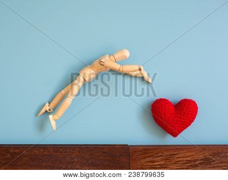 Wooden Puppet Jumping From The Wooden Floor In The Air To Catch The Red Heart Floating In The Sky. W