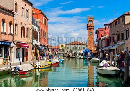 MURANO, ITALY - APRIL 20, 2016: People walking narrow canal with boats among old colorful houses of Murano - famous island in Venetian Lagoon, popular tourist destination.