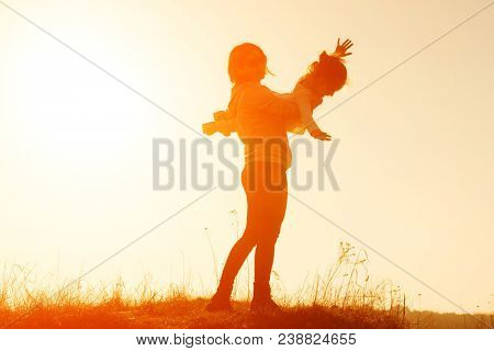 Happy mother raising her little daughter in the air. Mother and daughter playing airplane game at sunset. Mother and daughter silhouette