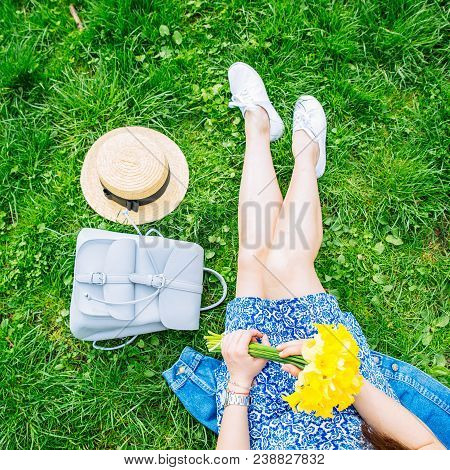 Woman Sitting On Grass In City Park With Yellow Flowers