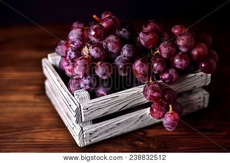 Branch Of A Dark Grapes In A White Box On A Wooden Background