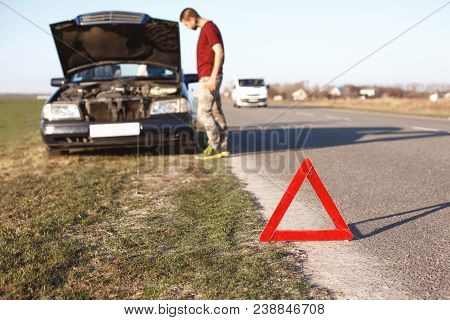 Car Breakdown Concept. Helpless Man Driver Stands Near Brocken Auto With Opened Hood, Has Problems W