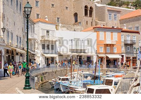 Tourists Walk Around The Small Boat Filled Harbor Ringed With Cafes, Restaurants And Shops - Hydra, 
