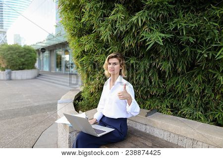Businesswoman Working With Laptop And Papers In Open Air Near Green Plant, Showing Thumbs Up. Concep